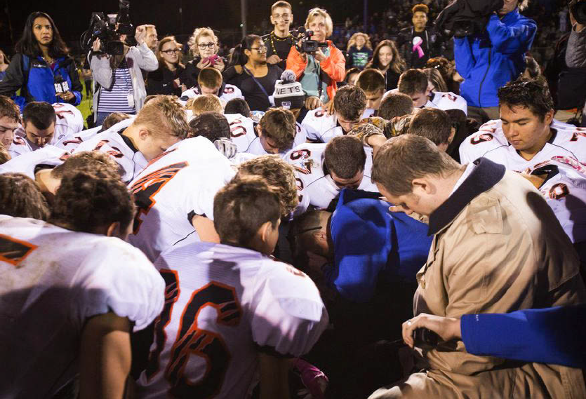 Coach Joe Kennedy praying with students