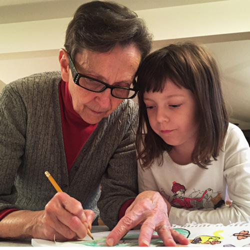 Photo of grandmother and granddaughter with heads together working on a school assignment