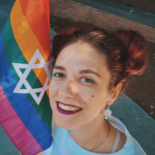 Smiling queer Jewish woman protected by religious freedom holding a Pride flag with the star of David on it