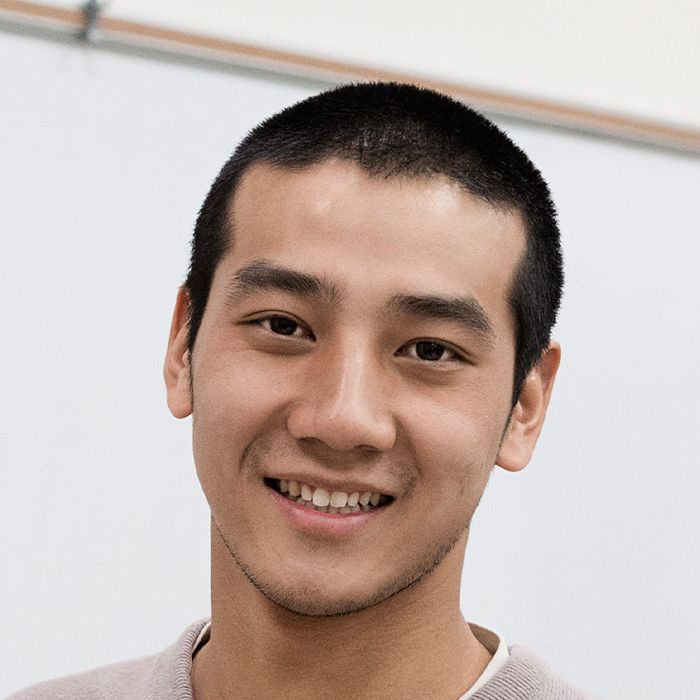 Young East Asian teacher smiling at camera in front of a white board