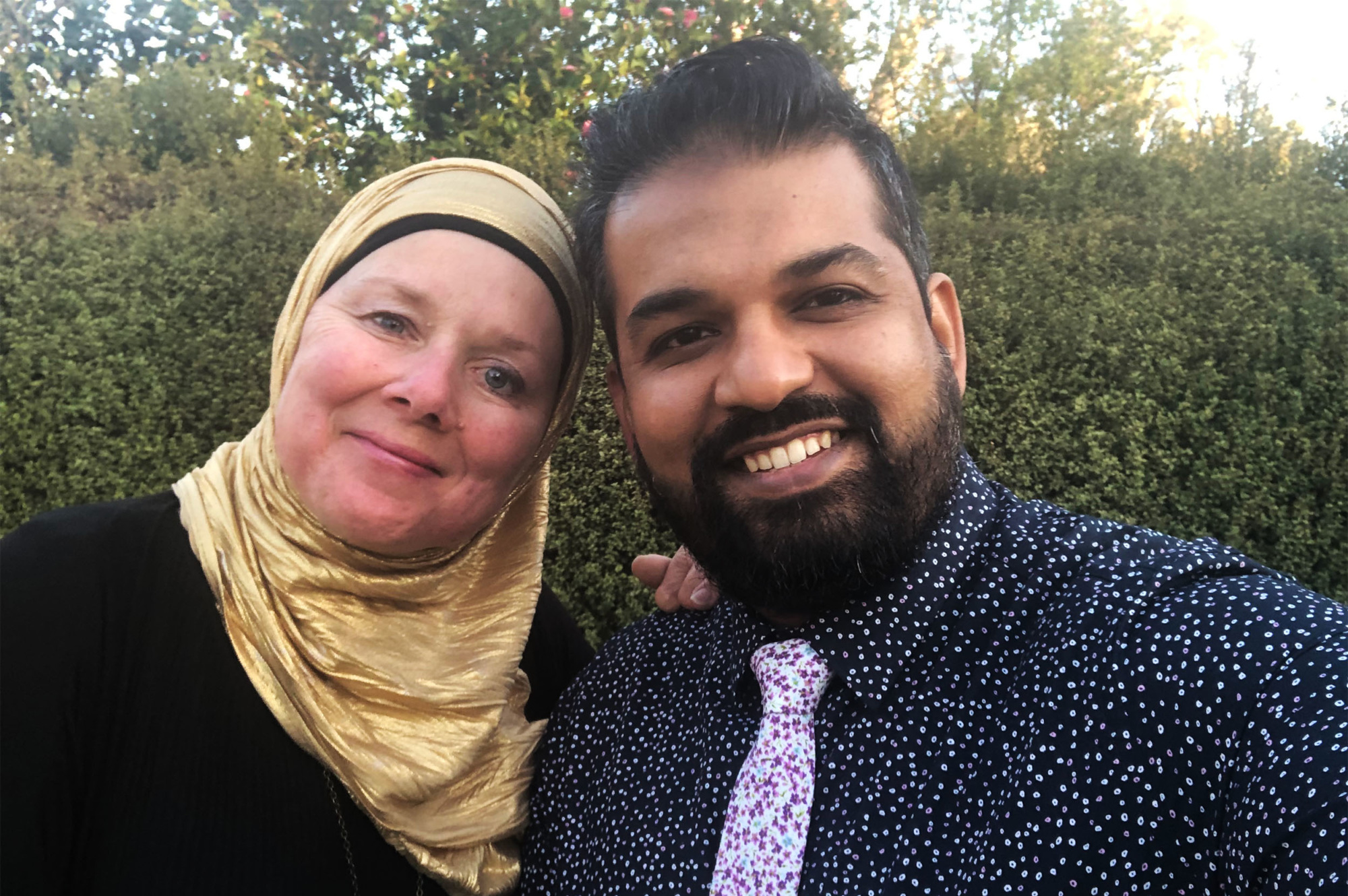 A woman wearing a hijab and a man in a flowered shirt and tie smile at the camera