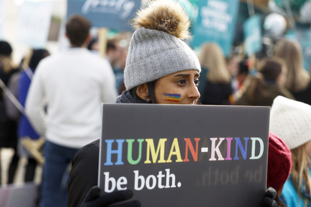 A protester holds a sign reading "Human-kind. Be both."