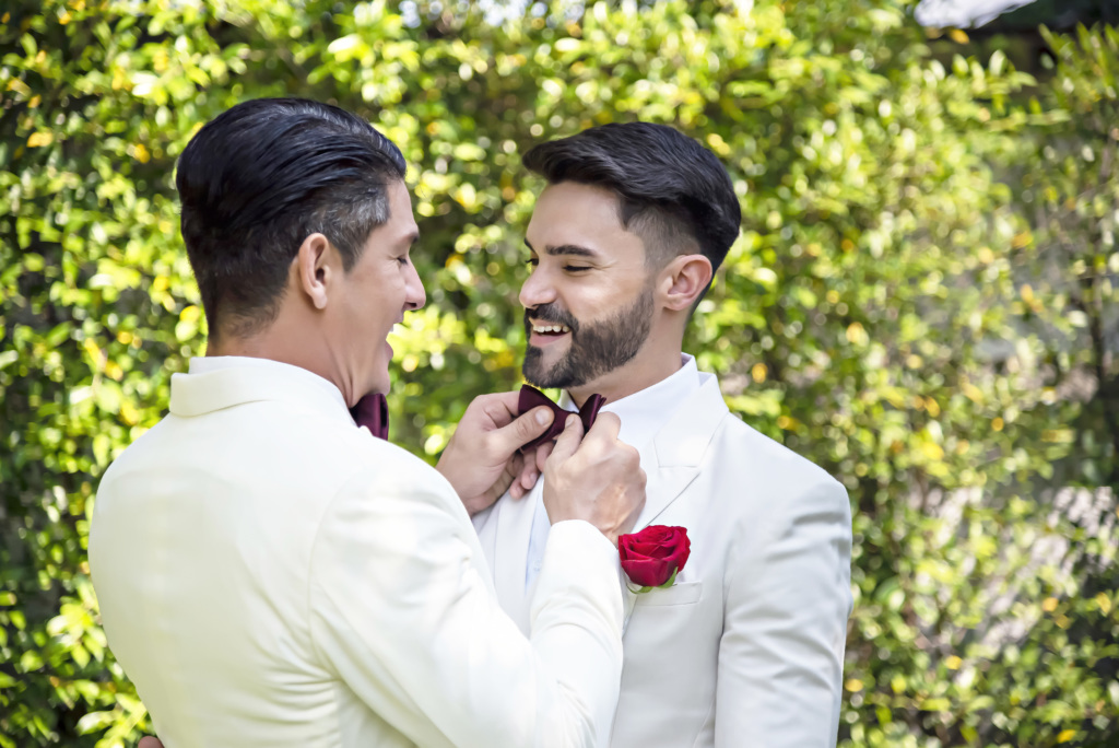 Same-sex couple gets ready for their wedding day, one lovingly adjusts the other's bowtie