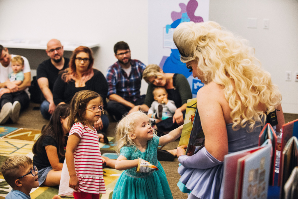 A drag queen reads a book to a crowd of young children and their parents.