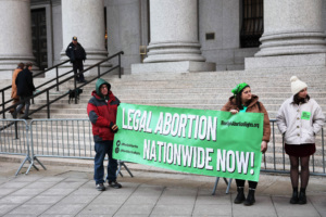 Protesters hold large green sign reading "Legal Abortion Nationwide Now!"