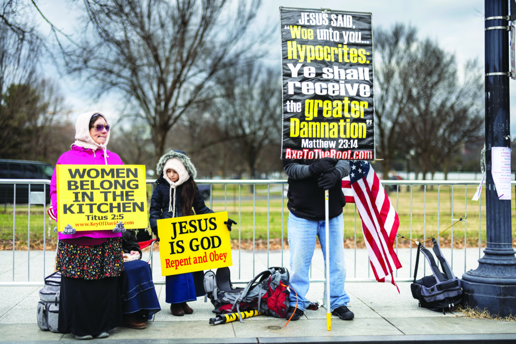 Pro-Trump protesters rally on January 6, 2021 with signs reading "Women Belong in the Kitchen" and "Jesus is God. Repend and obey."