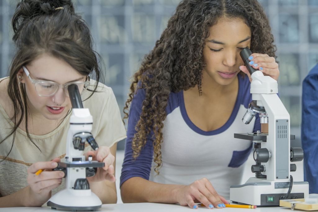 A multi-ethnic group of high school students are working in a science class together. They are looking at slides in biology class through a microscope.
